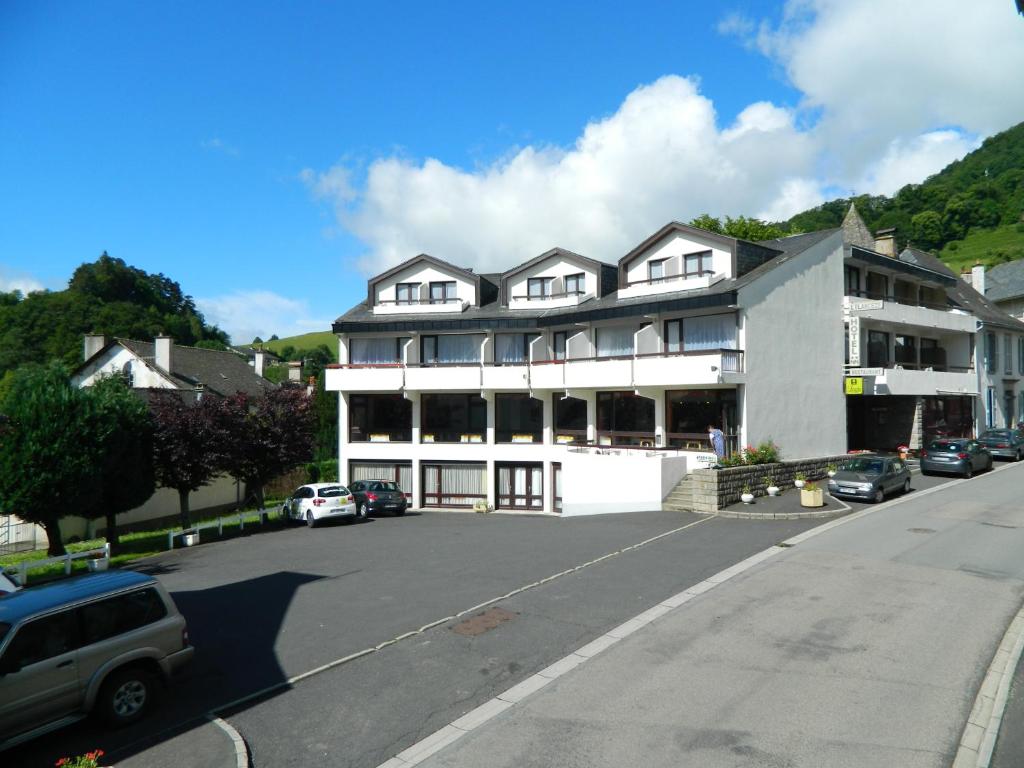 un grand bâtiment blanc avec des voitures garées dans un parking dans l'établissement L'Elancèze, à Thiézac