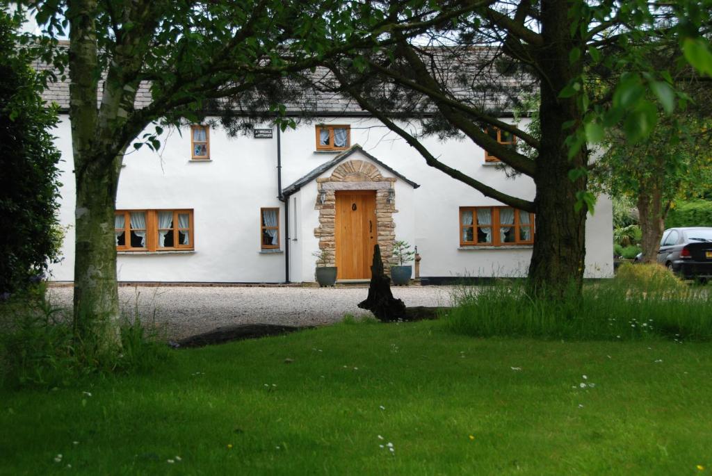 uma casa branca com uma porta castanha e árvores em Armidale Cottages B&B em Workington