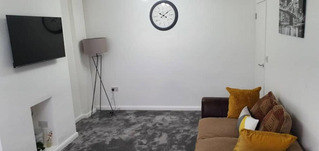a living room with a couch and a clock on the wall at Exquisite and Modern 2 bed Maisonette in Harmondsworth