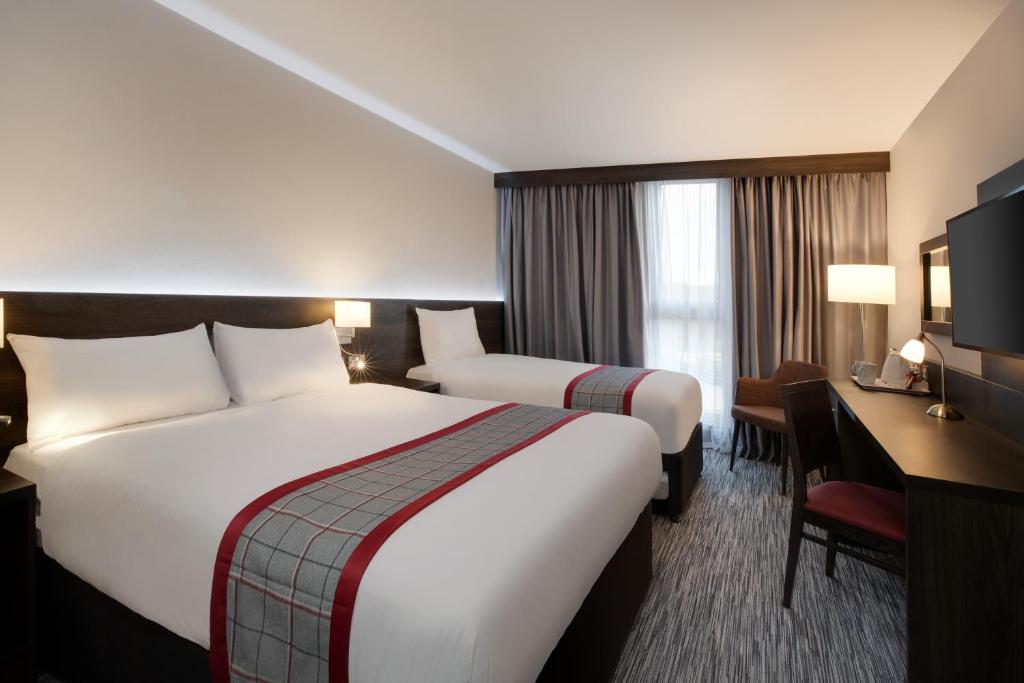 a hotel room with two beds and a desk at Ramada by Wyndham Leeds East in Leeds