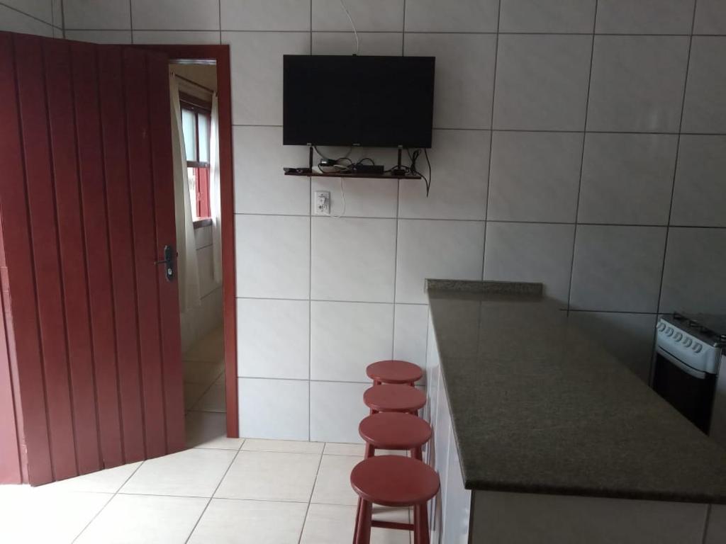 cocina con taburete y TV en la pared en Residencia Siqueira, en Garopaba