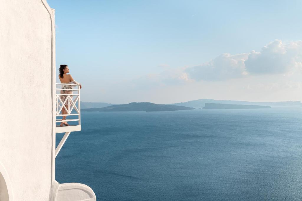 una mujer sentada en un balcón con vistas al océano en Caldera Premium Villas en Oia