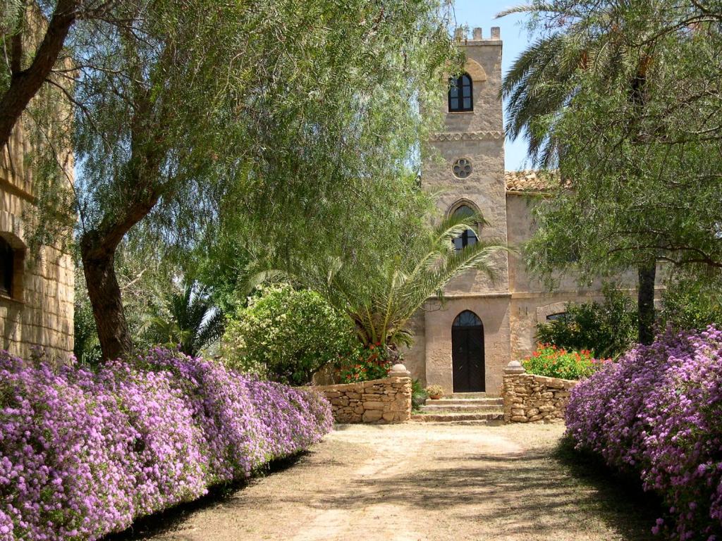 un jardin avec des fleurs violettes en face d'une église dans l'établissement Luxury Sicily Villas by Geocharme, à Castelvetrano