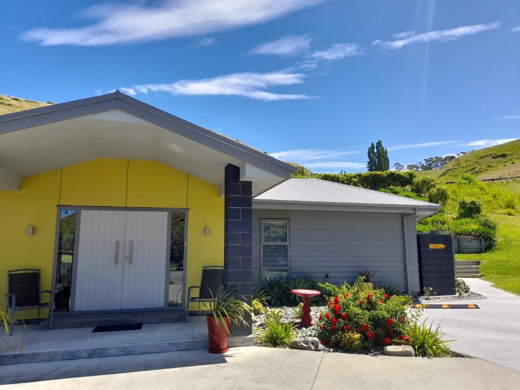 a yellow house with a white door and some flowers at Hidden Gem in Oaklands in Napier