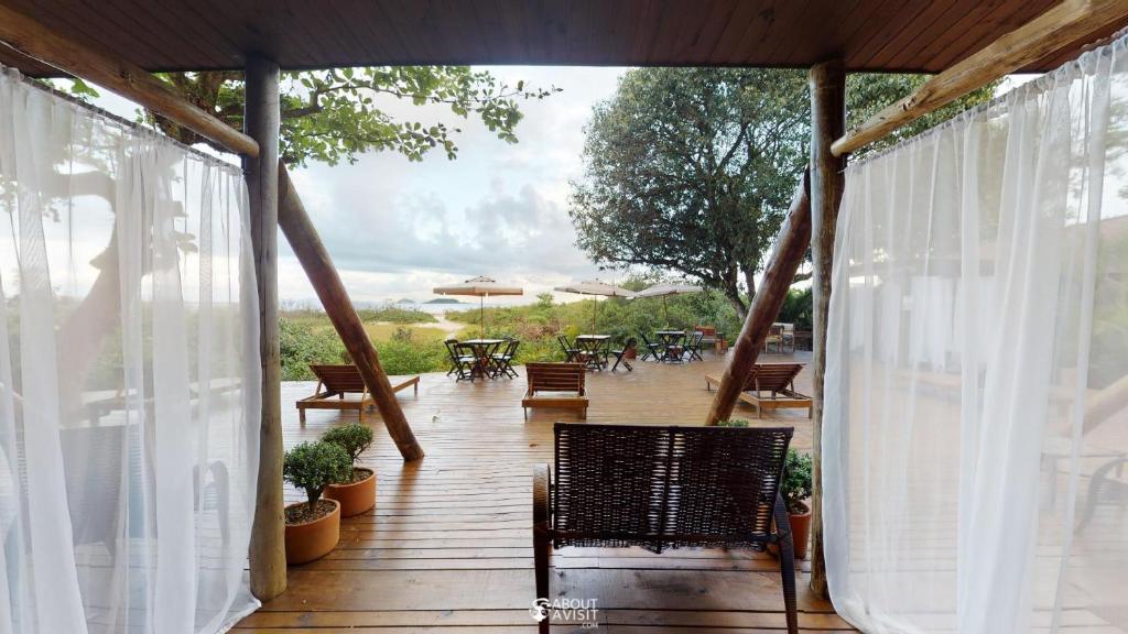 una terraza de madera con un banco, mesas y sillas en Pousada Villa Verde - Frente para a Praia do Farol, en Ilha do Mel