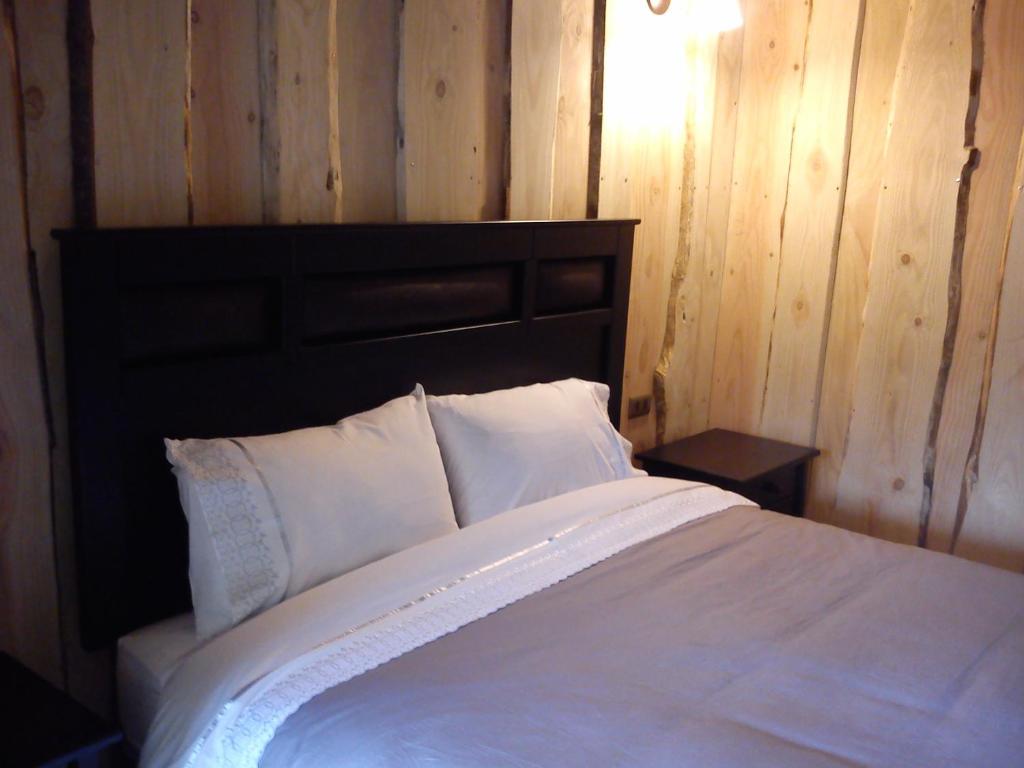 a bedroom with a white bed with a wooden wall at Hostal Los Alamos Neltume in Neltume