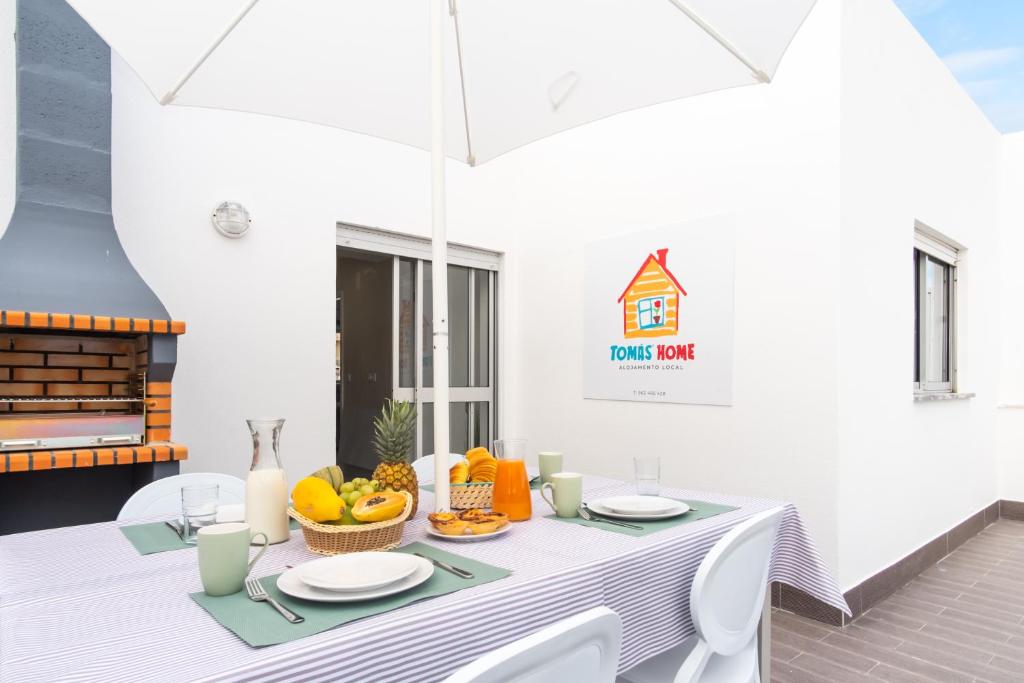 a white table with a white umbrella and fruits on it at TOMÁS HOME in Nazaré
