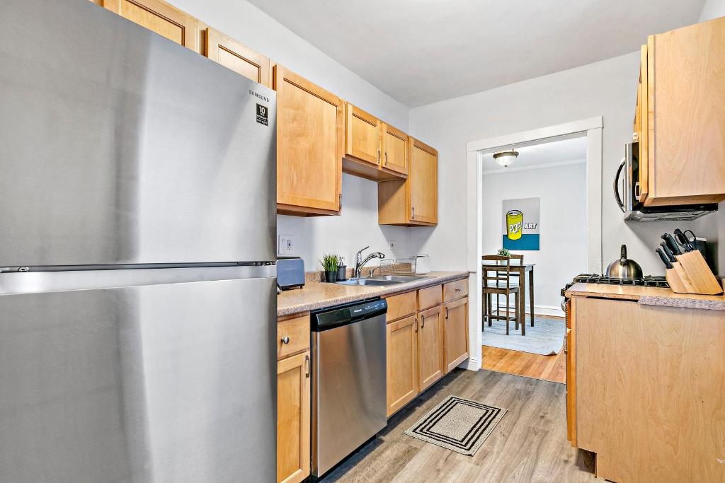 a kitchen with a stainless steel refrigerator and wooden cabinets at Chicago Local Vibe Residential 1BR Roscoe Village - Marshfield N3 in Chicago