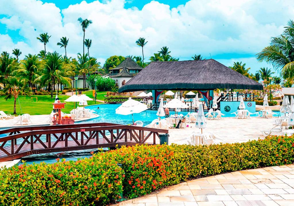 a resort pool with a bridge and chairs and umbrellas at Flat Beach Class Muro Alto 1107 in Porto De Galinhas