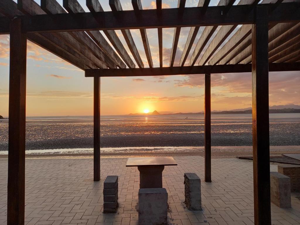 una puesta de sol sobre la playa con un banco en un pabellón en Apartamentos na Ponta dos Castelhanos - Anchieta en Anchieta