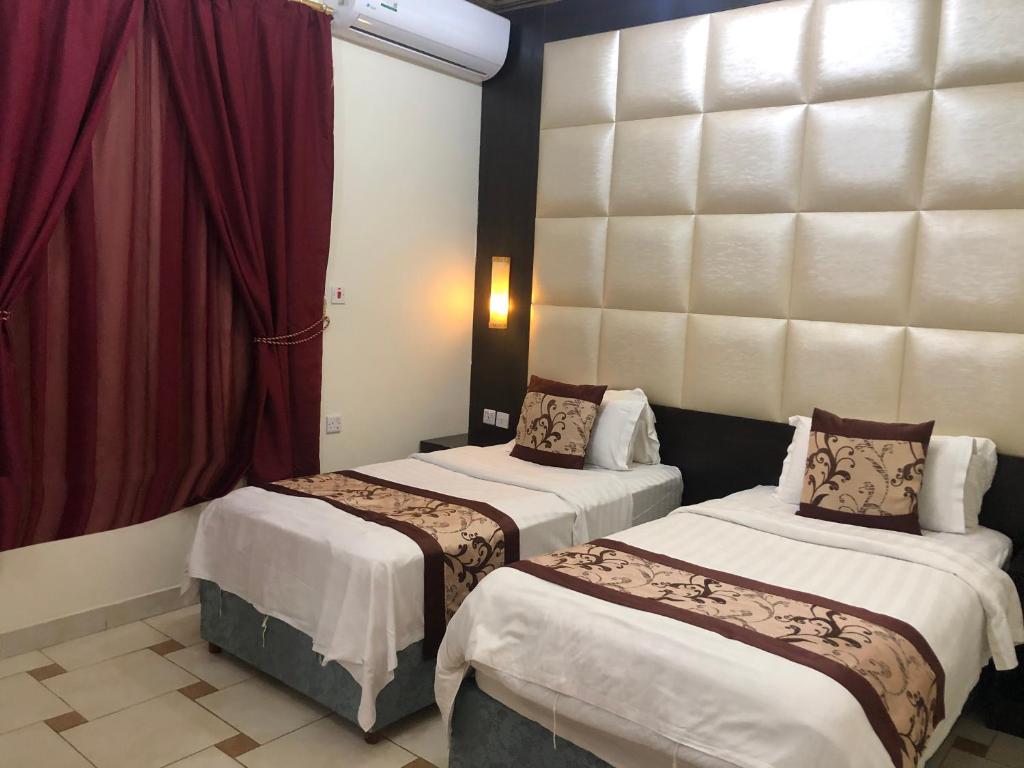 2 camas en una habitación de hotel con cortinas rojas en رايتنا للوحدات السكنية المفروشة, en Riad