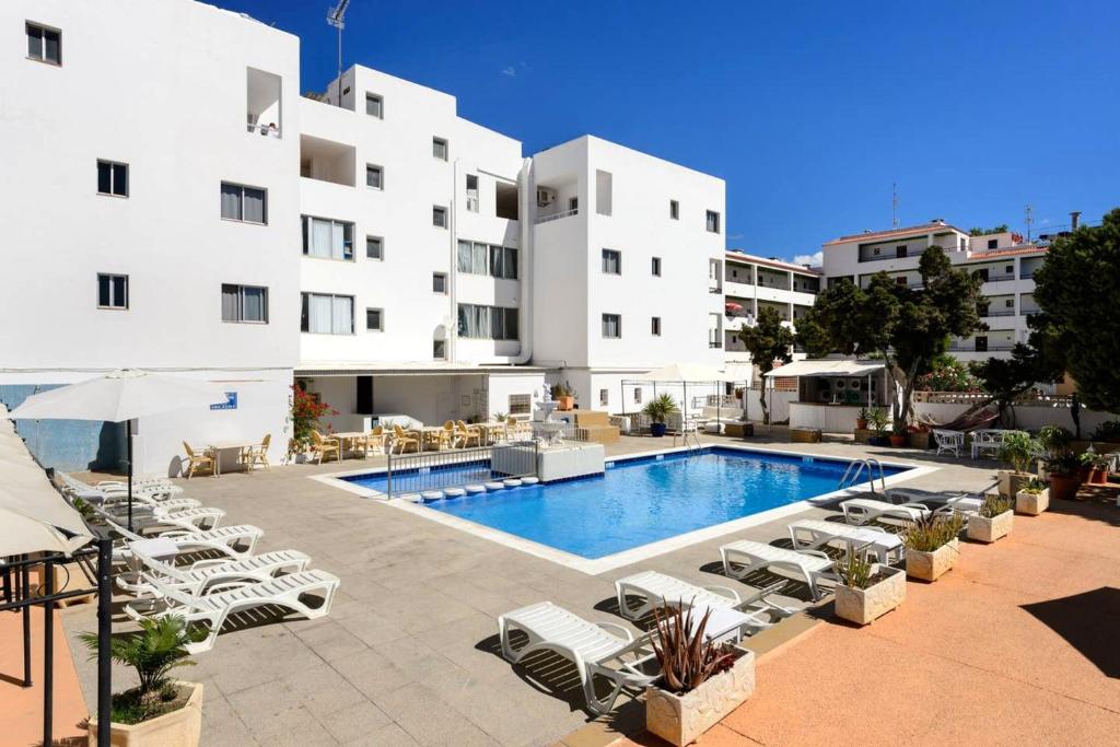 a hotel with a pool and chairs and a building at One bedroom apartement with sea view shared pool and furnished balcony at Sant Josep de sa Talaia in Sant Josep de Sa Talaia