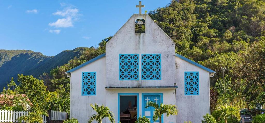 een kleine witte kerk met blauwe ramen en een kruis bij Appartement d'une chambre avec vue sur la mer piscine partagee et jardin amenage a Saint Joseph in Saint-Joseph