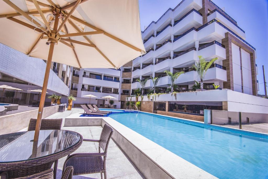 una piscina al aire libre con mesas, sillas y una sombrilla en GOLDFLAT - Cabo Branco by PenareiaTurBr, en João Pessoa