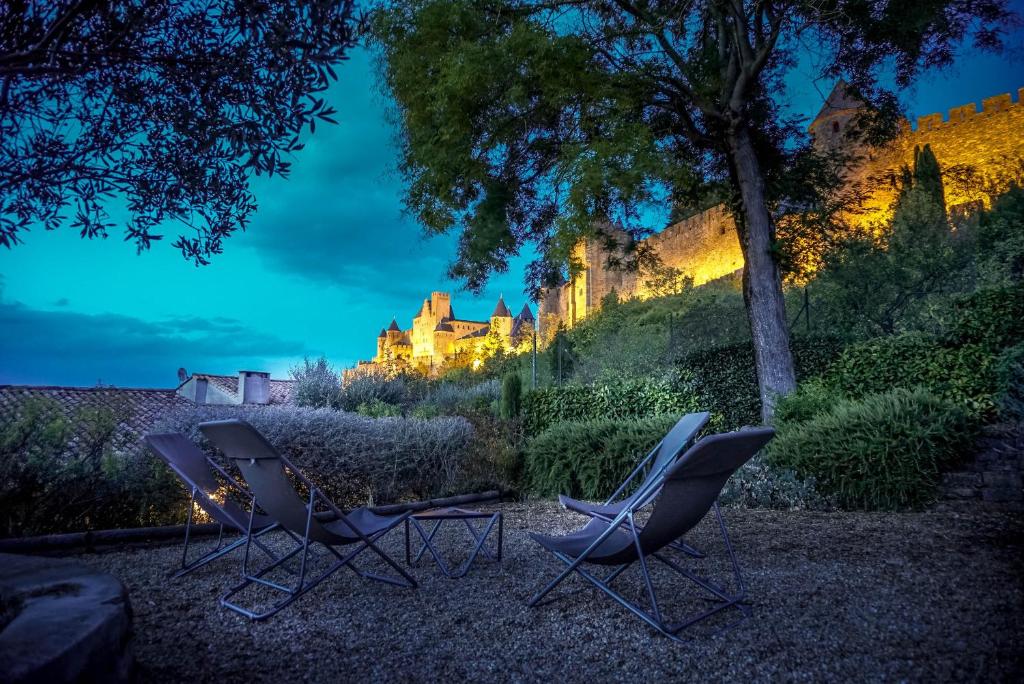 Trois chaises et un arbre avec un château en arrière-plan dans l'établissement Sous les courtines, à Carcassonne