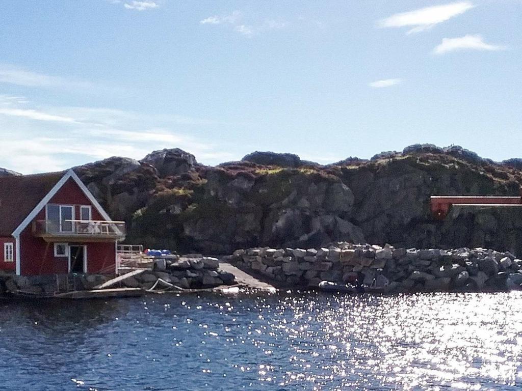 a red house on the water next to a mountain at 9 person holiday home in Utsira-By Traum in Utsira