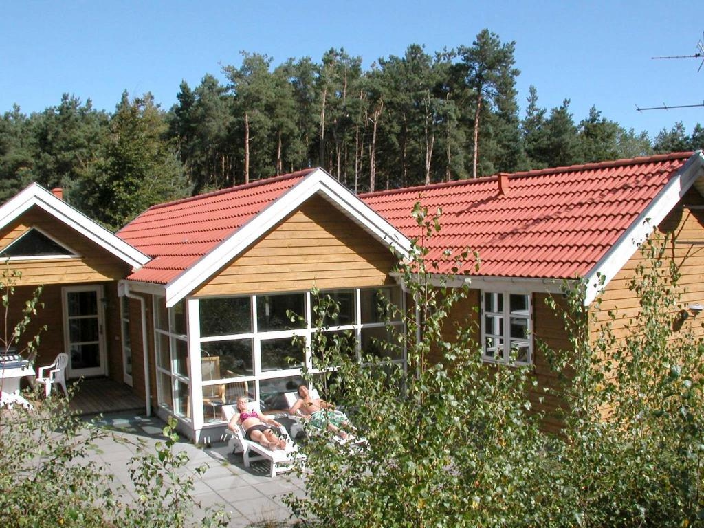 a house with a red roof and two people sitting on a patio at 10 person holiday home in Aakirkeby in Vester Sømarken