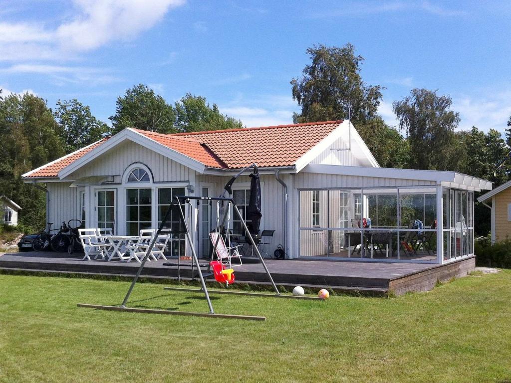 een klein wit huis met een speeltuin in de tuin bij 5 person holiday home in RONNEBY in Ronneby