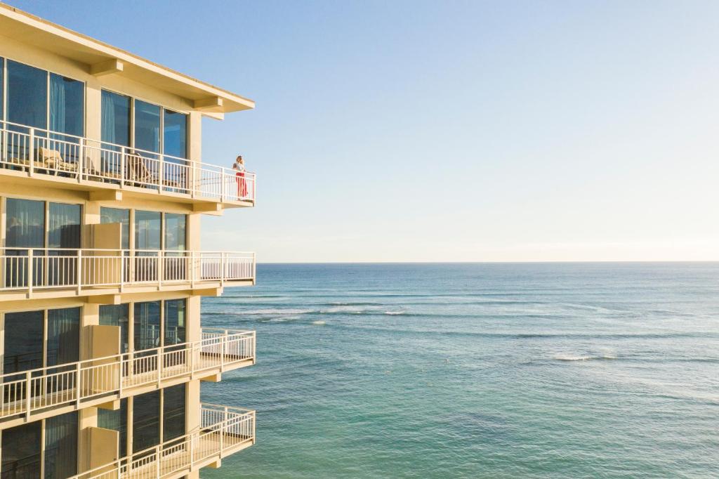 een gebouw met uitzicht op de oceaan en een persoon op het balkon bij Kaimana Beach Hotel in Honolulu