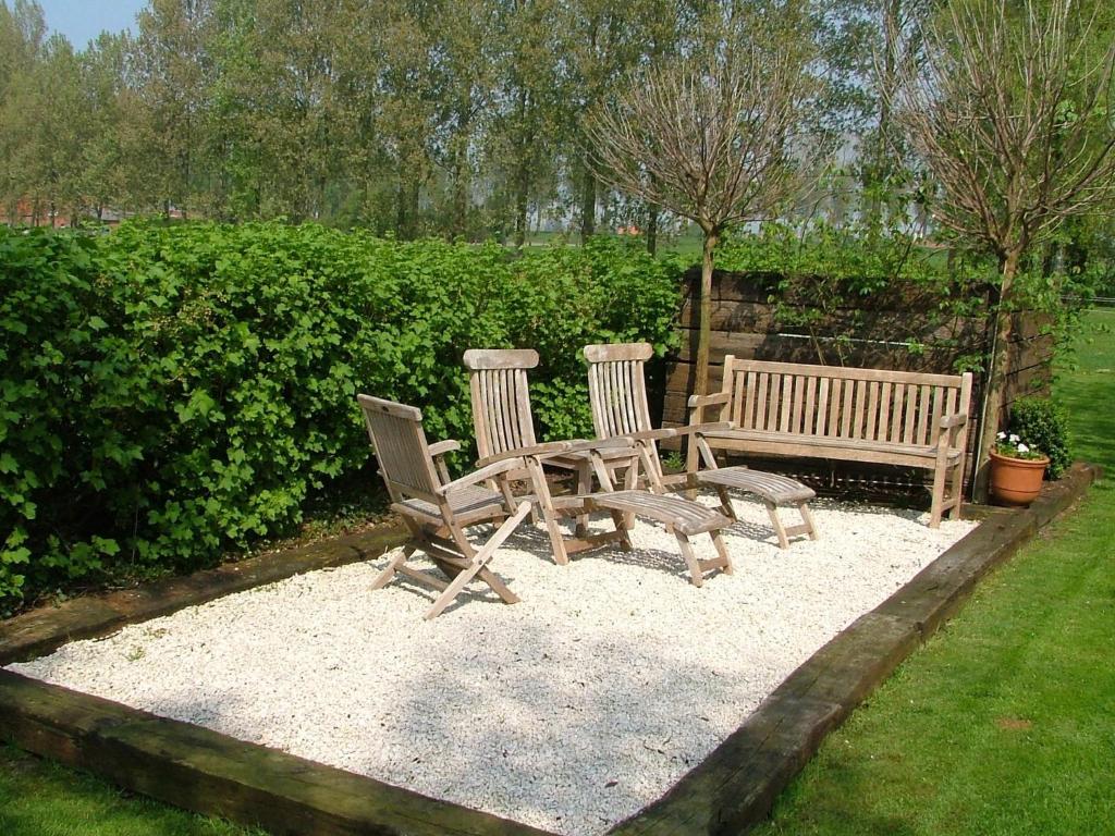 two wooden chairs and a bench in a garden at Cushy Apartment with Private Terrace Heating in Maldegem