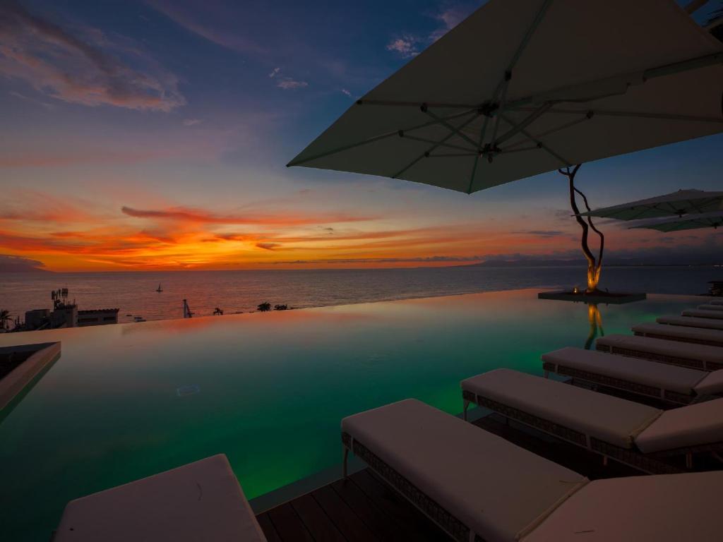 a pool with chairs and an umbrella and the ocean at PIER 57 - 709 Stunning View 2 BR Romantic Zone in Puerto Vallarta