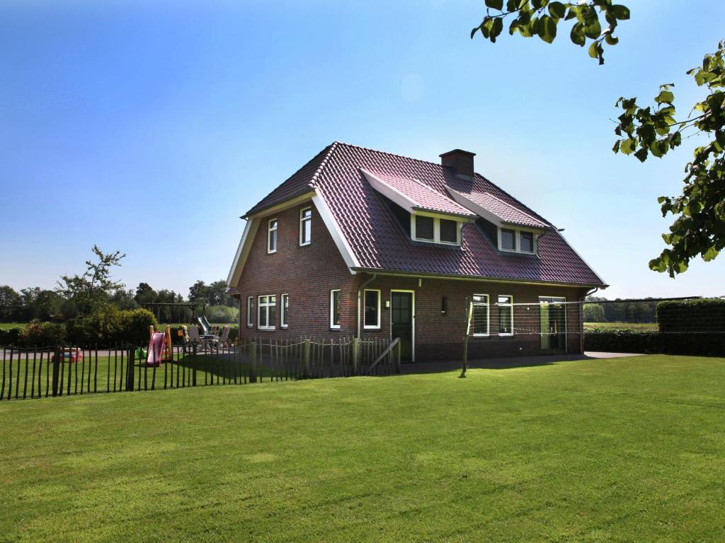 uma casa com um telhado vermelho num jardim verde em Spacious farmhouse in Achterhoek with play loft em Neede