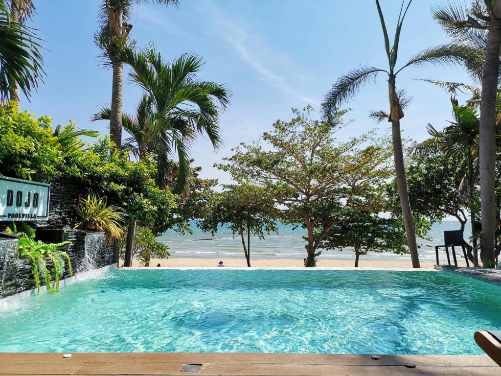 a large swimming pool next to a beach with palm trees at Dojo pool villa in Jomtien Beach
