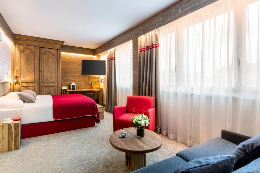 ジュネーヴにあるエーデルワイス マノテルのベッドと赤い椅子が備わるホテルルームです。