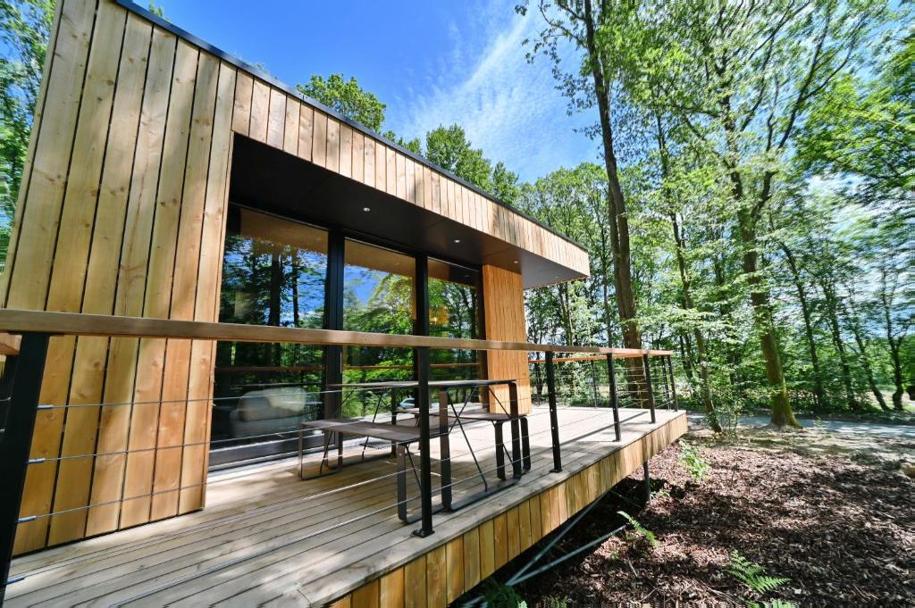 a wooden house with a deck in the woods at Forest Cube in Oignies-en-Thierache