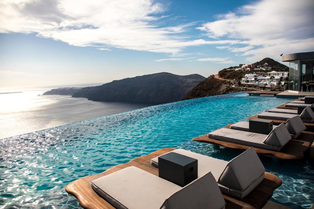 a infinity pool with lounge chairs and the ocean at Cavo Tagoo Santorini in Imerovigli