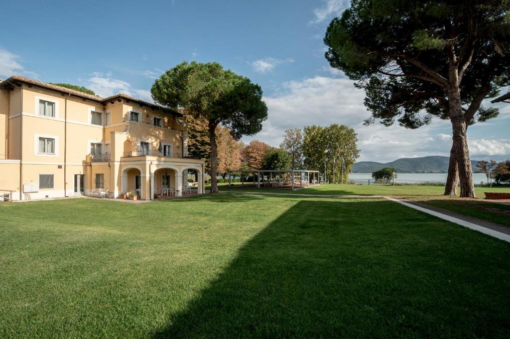 une grande maison sur un champ herbeux avec un arbre dans l'établissement Isola Polvese Resort, à Castiglione del Lago