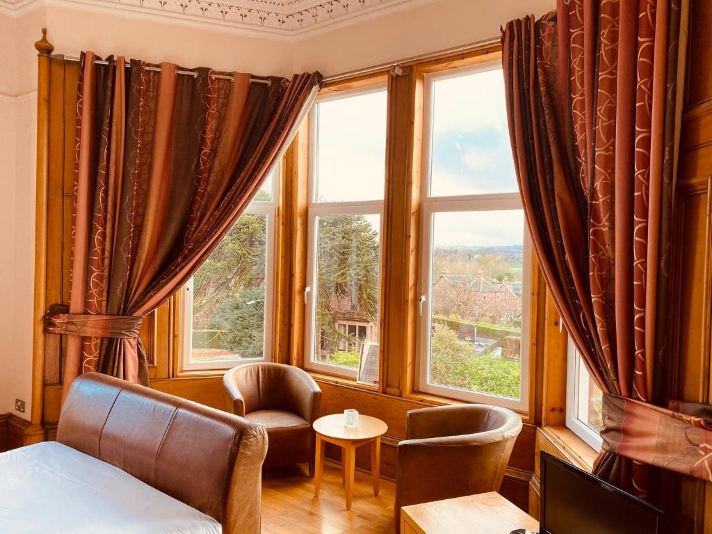 a bedroom with a bed and two chairs and windows at The Redstones Hotel & Restaurant in Glasgow