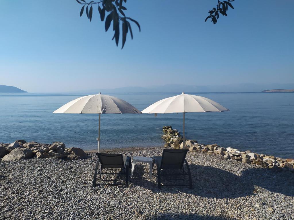 two chairs and a table and two umbrellas on a beach at Kalafatis beach home in Itea