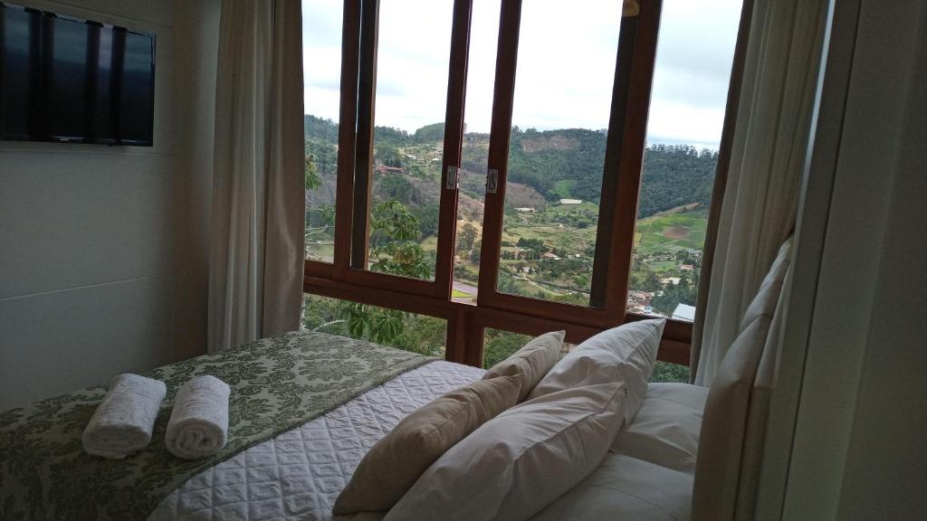 ein Schlafzimmer mit einem großen Fenster mit einem Bett und Kissen in der Unterkunft Apart Hotel Vista Azul - hospedagem nas montanhas in Domingos Martins