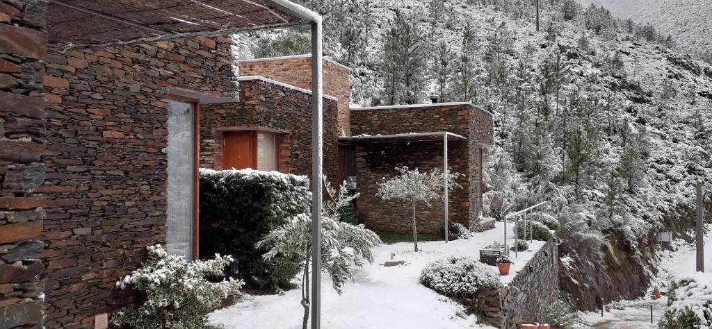 un edificio de ladrillo con nieve en el suelo delante en InXisto Lodges, en Piódão