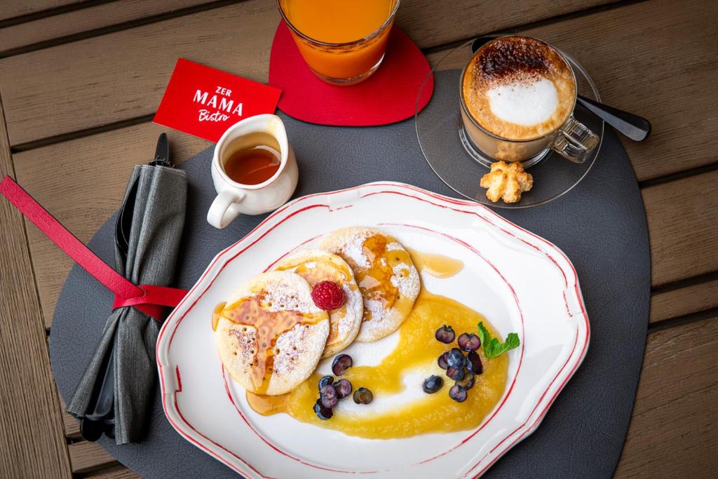 a table with a plate of pancakes and a cup of coffee at Hotel ZERMAMA Zermatt in Zermatt