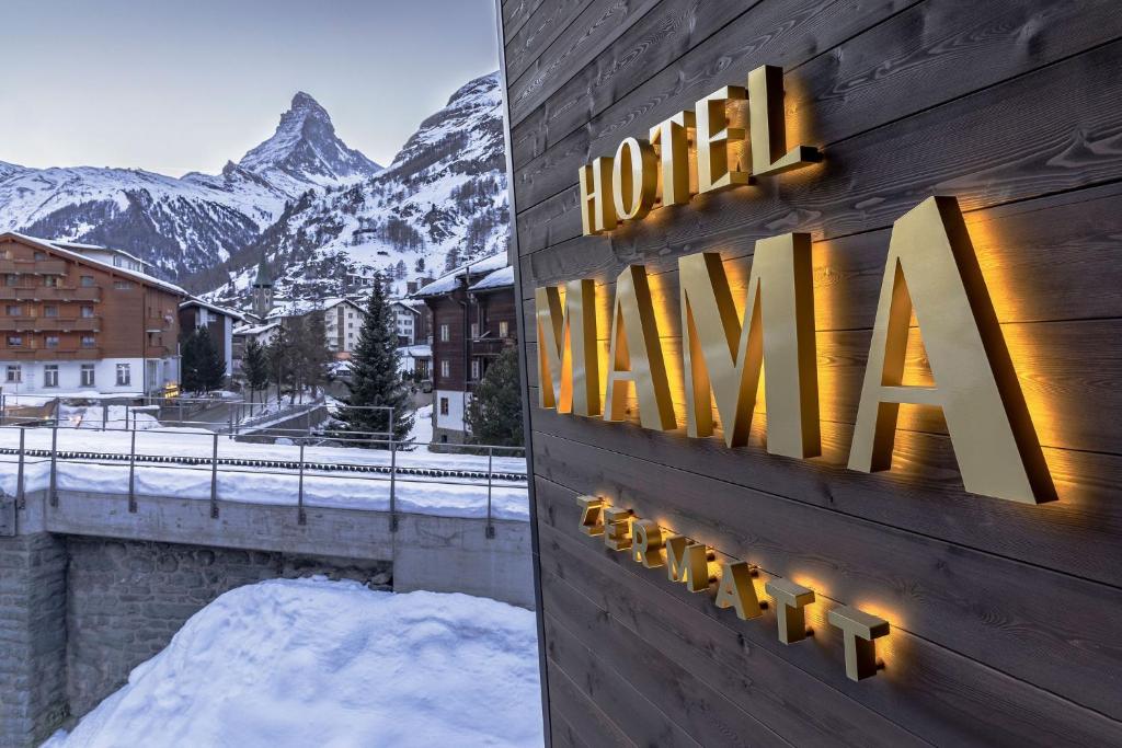 a hotel sign with a view of the mountains at Hotel ZERMAMA Zermatt in Zermatt