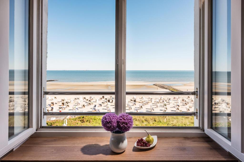 a window with a vase of flowers and a view of the beach at Strandhotel Gerken in Wangerooge