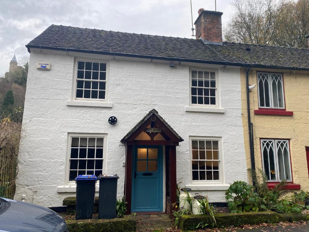 a white house with a blue door and two trash cans at Rock View Cottage, 2 bedrooms near Alton Towers in Alton