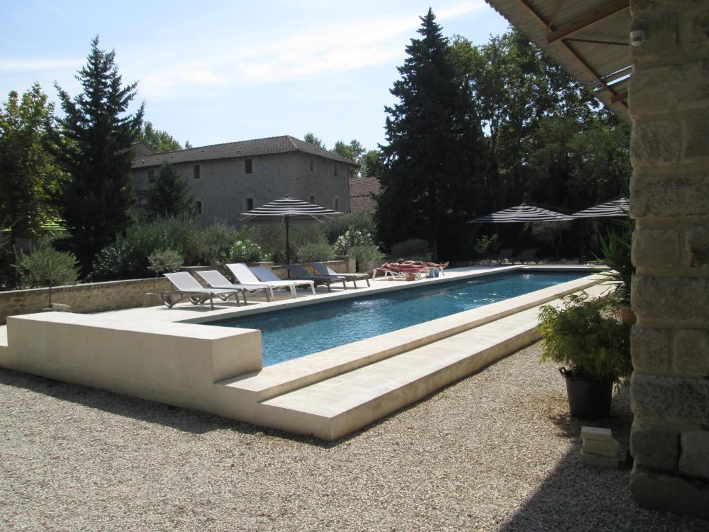 una piscina con bancos y sombrillas en un patio en Le Mas Vieux, en Graveson