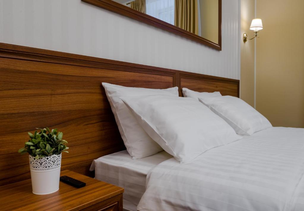 a bed with white pillows and a plant on a table at Отель МашБах in Cherepovets