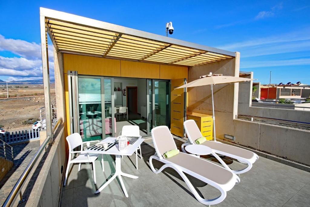 une terrasse avec des chaises blanches, une table et un parasol dans l'établissement LOS BALOS 29 by RENTMEDANO top level, spectacular ocean views, parking, wifi, à El Médano