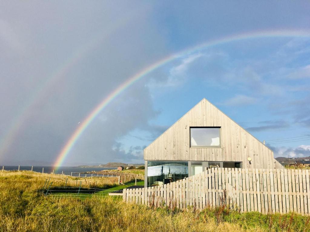 a rainbow over a wooden house with a fence at Luxury coastal retreat with stunning views in Aultbea