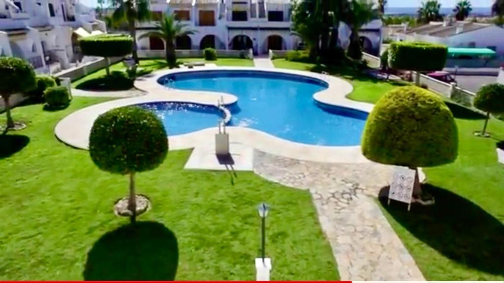 uma piscina num quintal com árvores e um edifício em 2-Bed Apartment 10 min drive to the Beach! em Ciudad Quesada