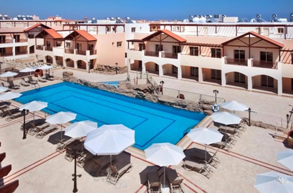 a swimming pool with umbrellas and tables and buildings at 2 bedrooms apartement with shared pool furnished terrace and wifi at Larnaca 2 km away from the beach in Tersephanou