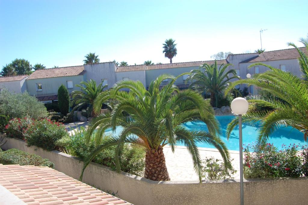 a pool with palm trees in front of a building at Appartement cosy à Valras-Plage / 48m² / Piscine partagée in Valras-Plage