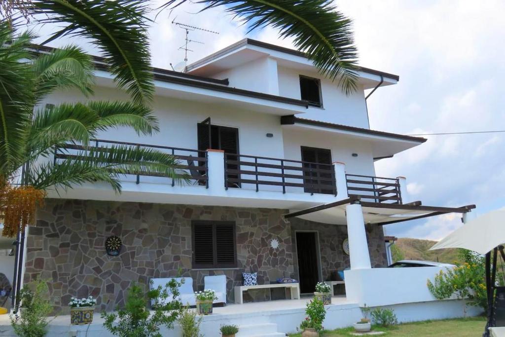 uma casa branca com palmeiras em frente em 5 bedrooms house at Brancaleone Marina 200 m away from the beach with sea view jacuzzi and enclosed garden em Brancaleone Marina