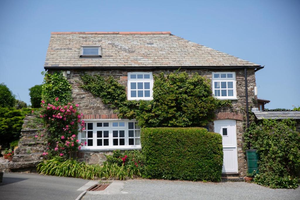 una casa de piedra con flores a un lado. en Coach House, en Bude