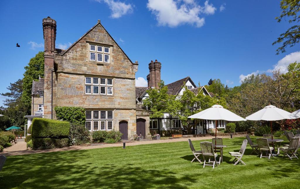 una casa con sillas de césped y sombrillas delante de ella en Ockenden Manor Hotel & Spa, en Cuckfield