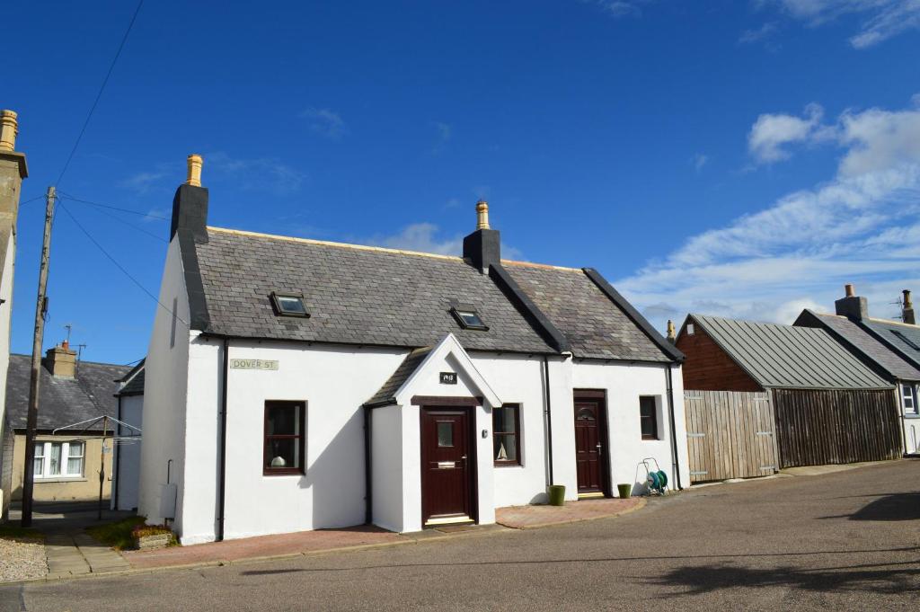 un bâtiment blanc avec un toit noir dans une rue dans l'établissement 4-Bed Cottage in Portknockie Near Cullen Moray, à Portknockie